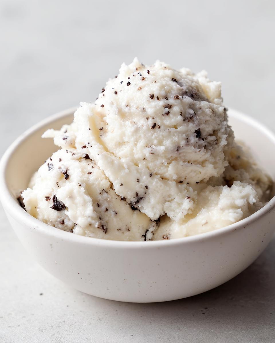 A close-up of a scoop of creamy Vanilla bean rice pudding speckled with dark vanilla bean seeds in a white bowl.
