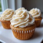 Close-up of a perfectly baked vanilla cupcake with generous swirls of creamy vanilla buttercream frosting.