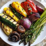 A close-up of a vibrant grilled vegetable platter featuring zucchini, yellow squash, peppers, red onion, mushrooms, and asparagus.