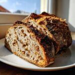Two thick slices of freshly baked Walnut sourdough bread showing an open crumb structure filled with walnuts.