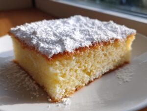 A close-up of a square slice of moist Warm milk cake topped generously with white powdered sugar.